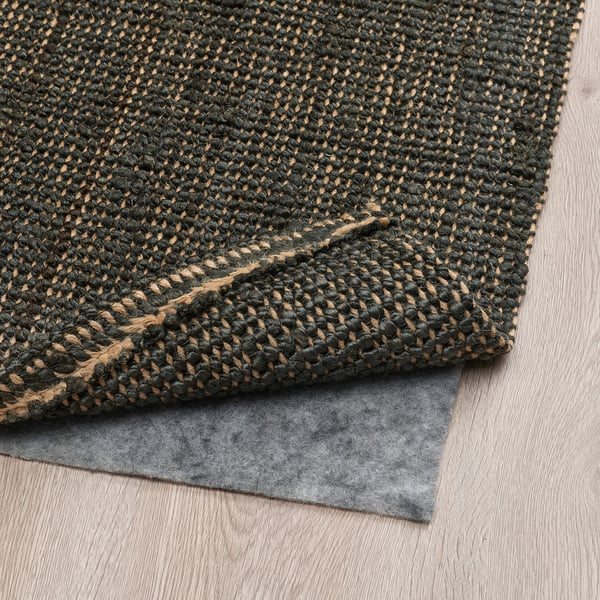 Dark green jute rug on wood floor, grey underlay, flat-woven for easy maintenance and heating.