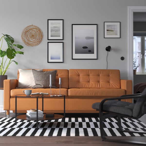 Modern living room: large tan leather landskröna sofa, striped rug, black chair, art wall, plant.