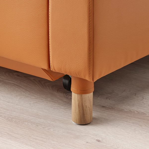 An orange leather sofa with wooden legs on a wooden floor.