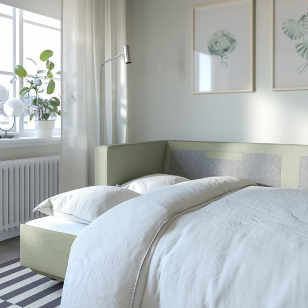 Bedroom with LANDSKRONA sofa bed, light covers, green headboard, white sheets, striped rug, plant, and framed art on wall.