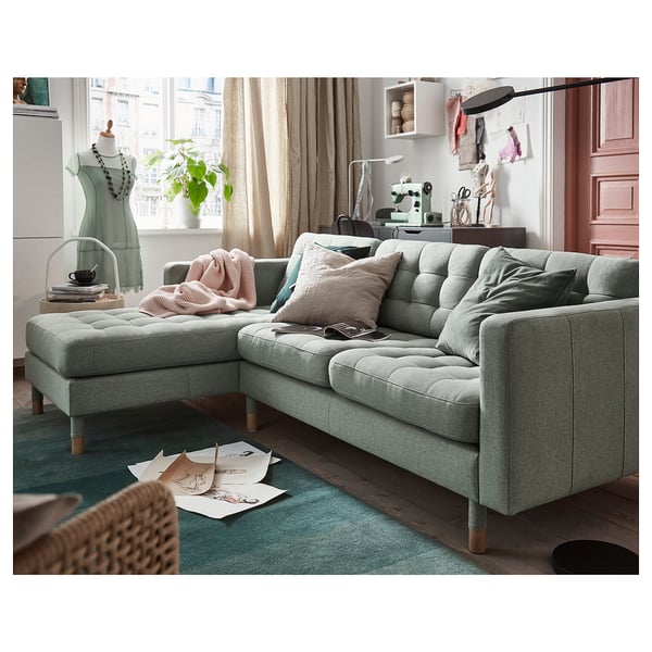 Modern living room with LANDSKRONA l-shape sofa, pink/gray pillows, green rug, sewing machine.