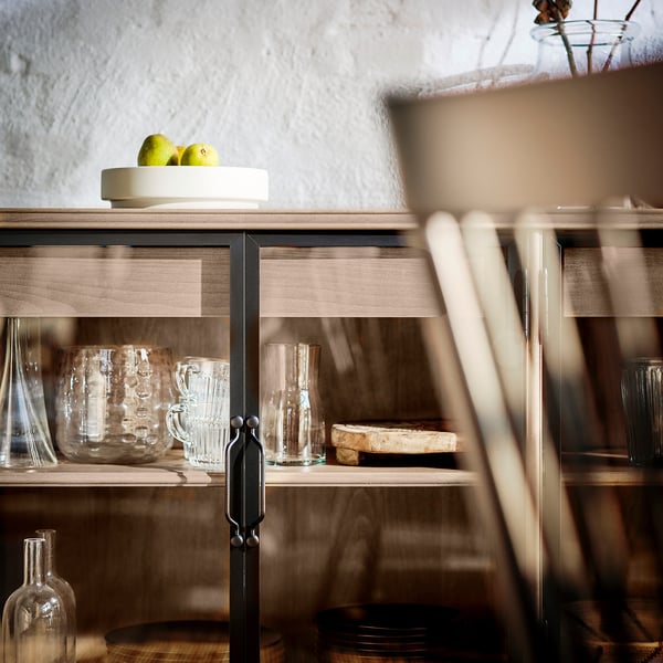 Wooden cabinet with glass doors stores clear glasses and dishes, a bowl of green apples on top.
