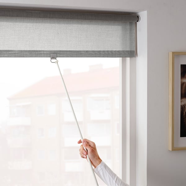 Pulling blind cord, partially covering window indoors.
