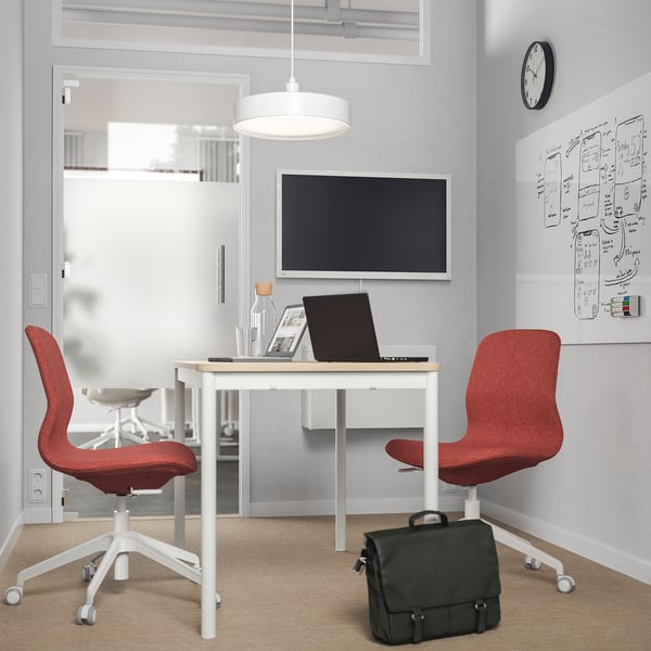 Small home office with LÅNGFJÄLL chair, laptop, tv, and whiteboard. Red chair, black bag, white desk, grey walls.