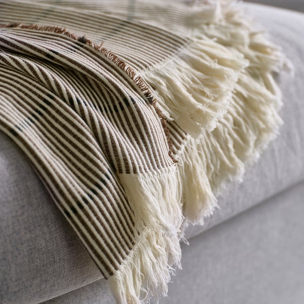 A fringed throw blanket, folded neatly, showcasing its striped brown/black pattern and soft cotton texture.