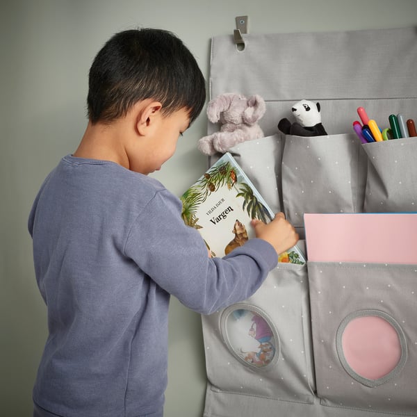 Child reaching for book in hanging organiser with pockets and toys.