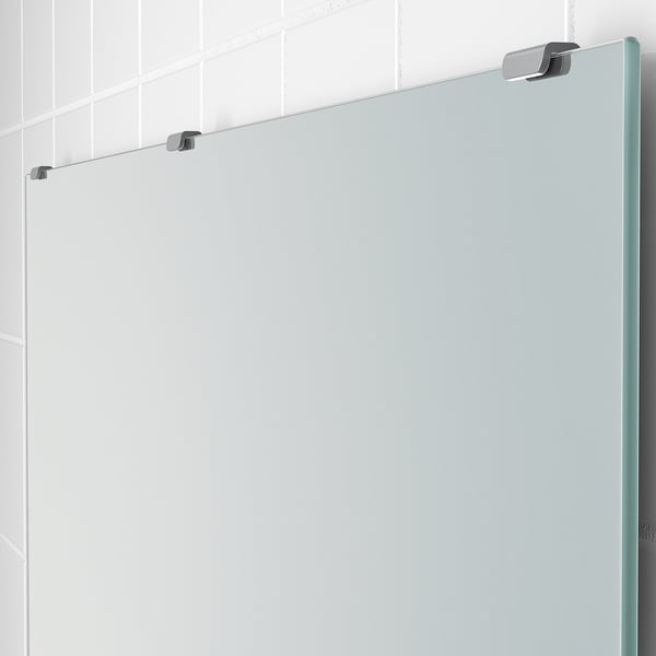 Modern, frameless mirror mounted with adjustable metal fittings, reflecting a tiled wall.