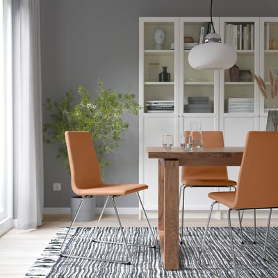 Modern dining area with wooden table, 4 LILLÅNÄS chairs, chrome sled bases, grey rug, pendant light, large plant, and a bookshelf.