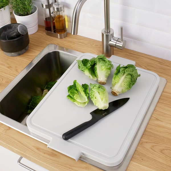 Metal sink with LILLHAVET cutting board on top, holding lettuce and knife.