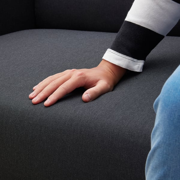 Person sitting on a black LINANÄS sofa, wearing a black and white striped shirt. Hand rests on arm.