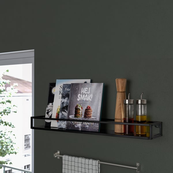 Black wall shelf holding cookbooks, spices, and a wooden pepper grinder near a window.
