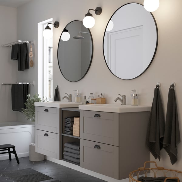 Modern bathroom with large round lindby mirrors, dark frames, vanity & wall lights. Decorated with towels, plants & baskets.