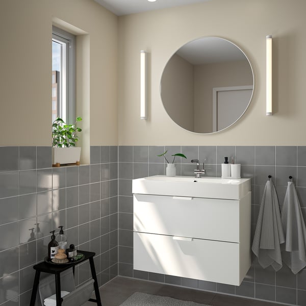 Modern bathroom with large white round LINDBYN mirror, broad vanity, grey tiles, and hanging towels.