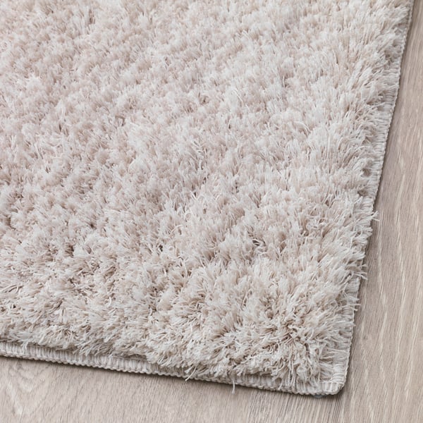 Fluffy beige rug, plush soft fibres, dense pile, lays flat on floor, recycled materials, cosy, noise-reducing.