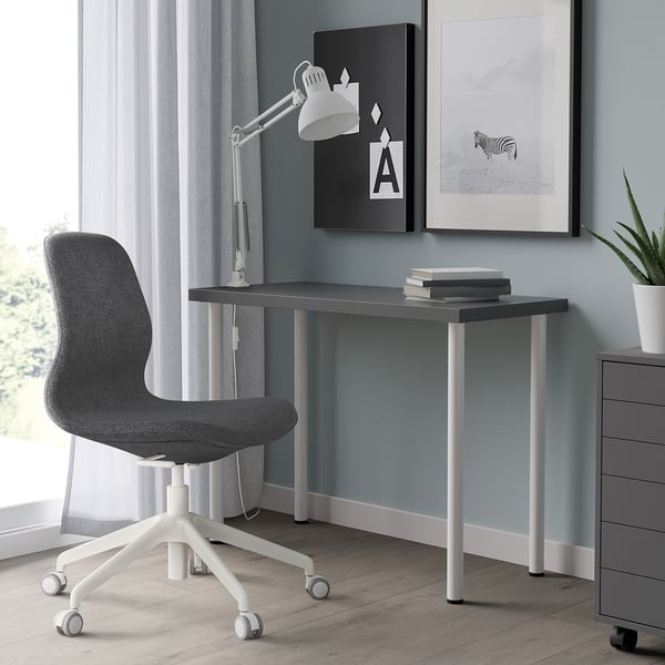 Modern home office setup with grey LINNMON desk & grey office chair, white lamp, & plant. Desk smaller than other items.