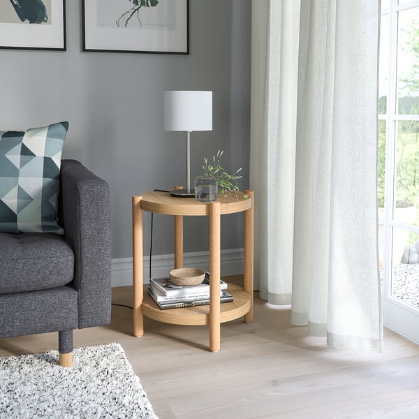 Round wooden LISTERBY side table. Light brown, simple design, beside grey chair and white lamp.