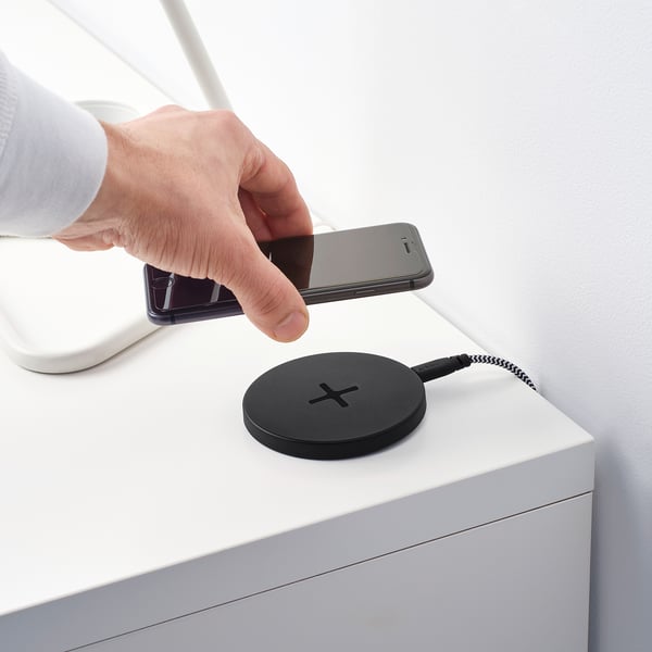 Image shows a person placing a smartphone on a round black wireless LIVBOJ charging pad, demonstrating its wireless charging function.