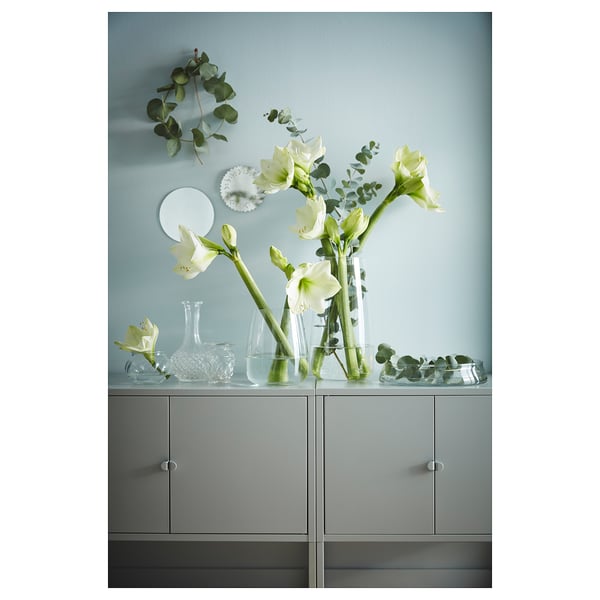 White flowers in clear vases on grey storage cabinet.