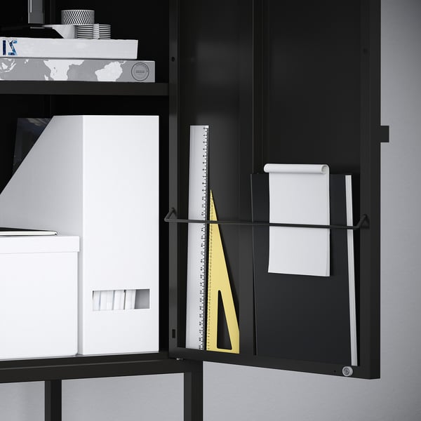 Black storage cabinet with adjustable shelf, holding white folders, a ruler, and a paper towel holder, showcasing its organisational.