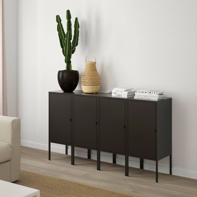 Black sideboard with 4 doors, cactus, basket, books. Between armchair and wall.