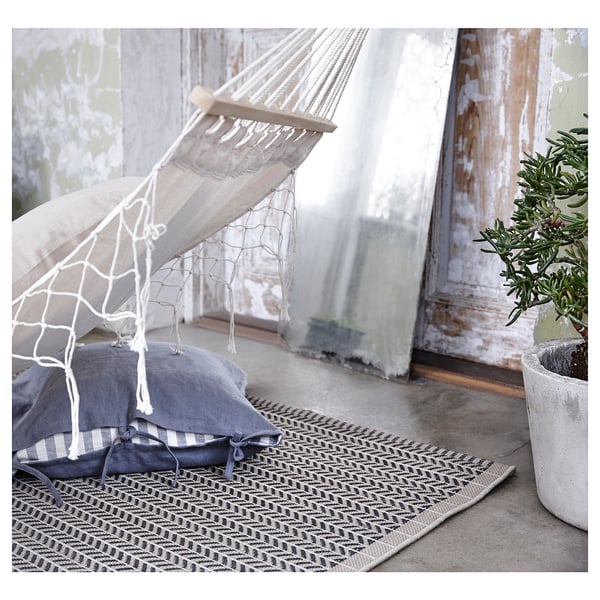 Cosy indoor scene, hammock with blue pillows, patterned rug, and potted plant beside distressed door.