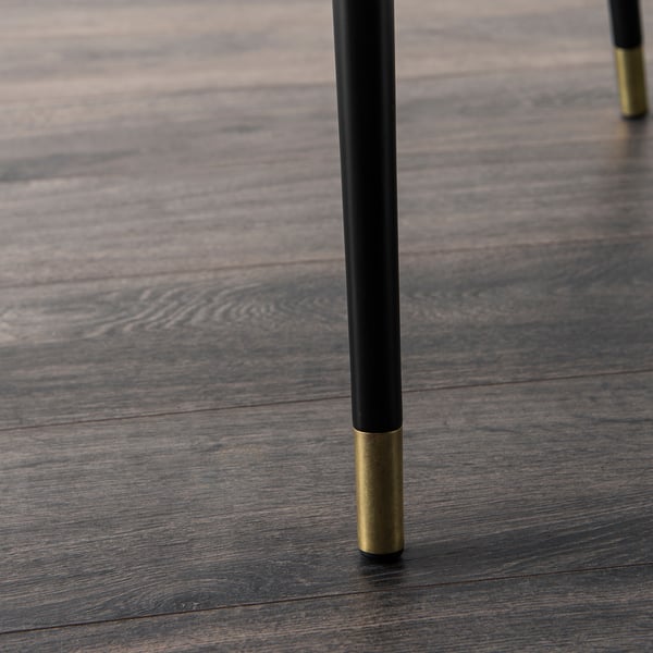 Close-up of black table leg with gold-tone tip on wooden floor.