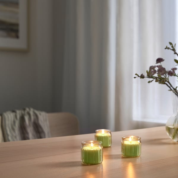 Three candles on a wooden table with apple scent and flowers in the background.