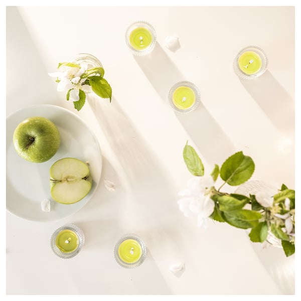 Six green candles around a green apple and slice on white plate with flowers.
