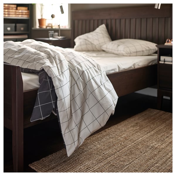Beige jute rug under bed with grid print white blanket on bed.