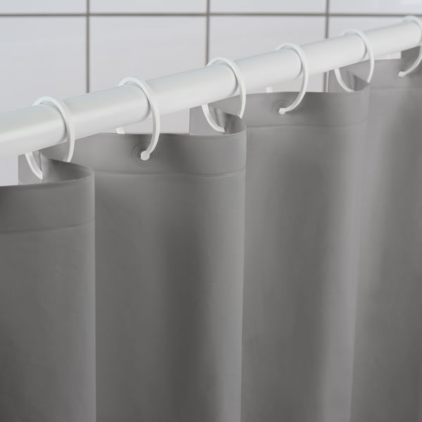 Grey shower curtain hangs from white hooks and rod, demonstrating its water-repellent and durable design.