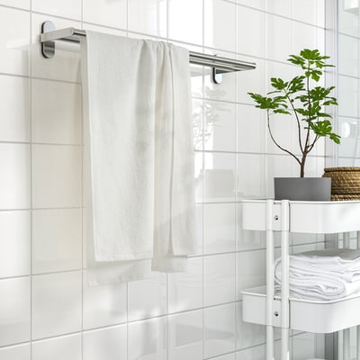White ludvial towel on steel rack in a bathroom with white tiles and shelving.