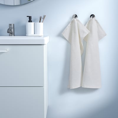 A white LUDDVIAL towel hung on hooks next to a bathroom vanity. The towel is rectangular, made of cotton, and appears smaller than the vanity.