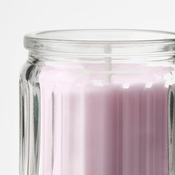 A close-up of a clear glass jar with a ribbed texture, containing a bright pink scented candle inside.