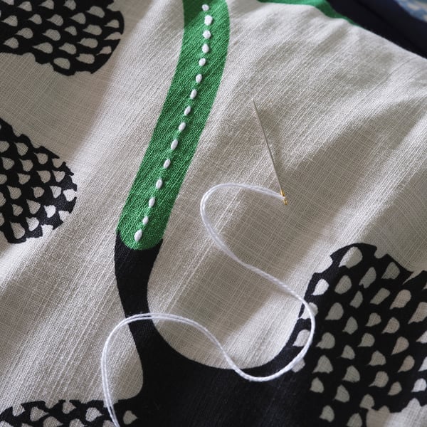 Close-up of patterned fabric with sewing needle and thread, showcasing intricate stitching and detailed design.