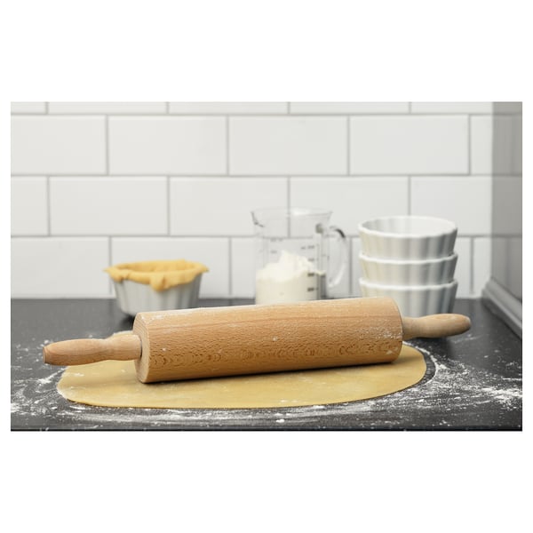Wooden rolling pin on rolled dough, kitchen utensils, white tiled wall.
