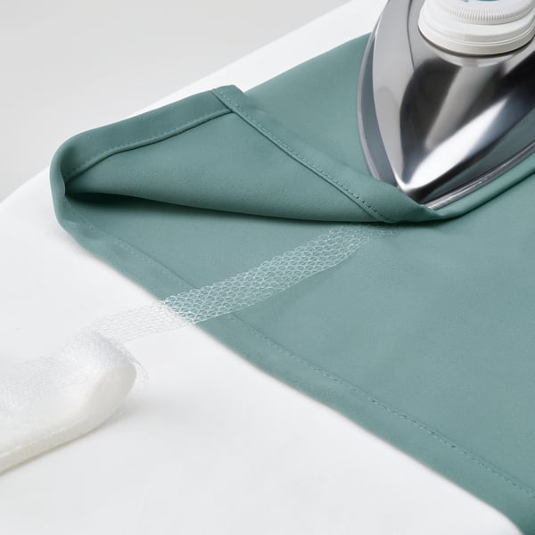 Silver iron pressing teal MAJGULL curtains on white surface, showing steam and wrinkle resistance.