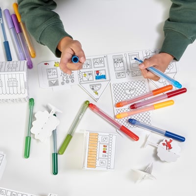 In a person is crafting a town using MÅLA cardboard templates and marki pens, demonstrating creativity and fine motor skills.