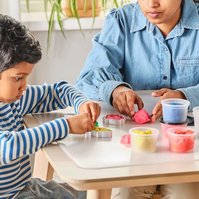 Two people playing with colourful modelling dough and cookie cutters.