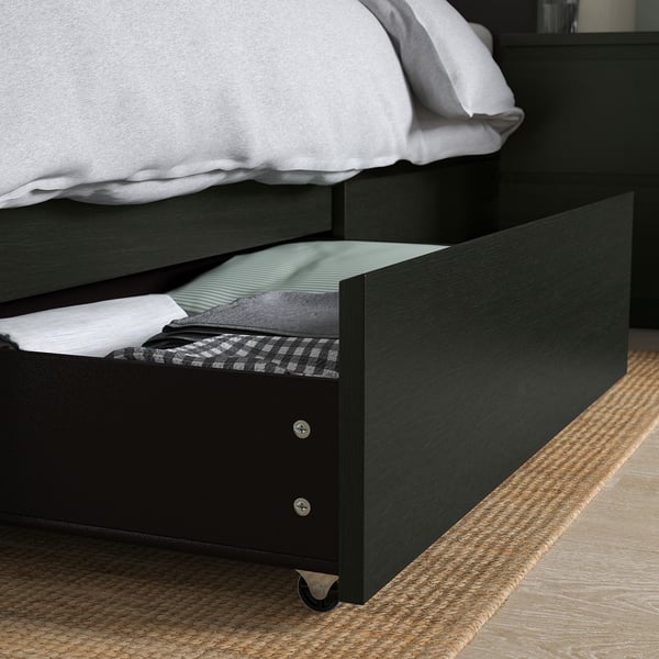 Black bed frame with open drawer, showing blankets & pillows. MALM series with under-bed storage drawers.