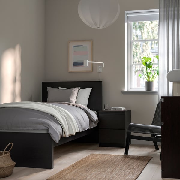 Modern bedroom with grey MALM bed, white pillows, black bedside table, art, pendant light, and window with plant.