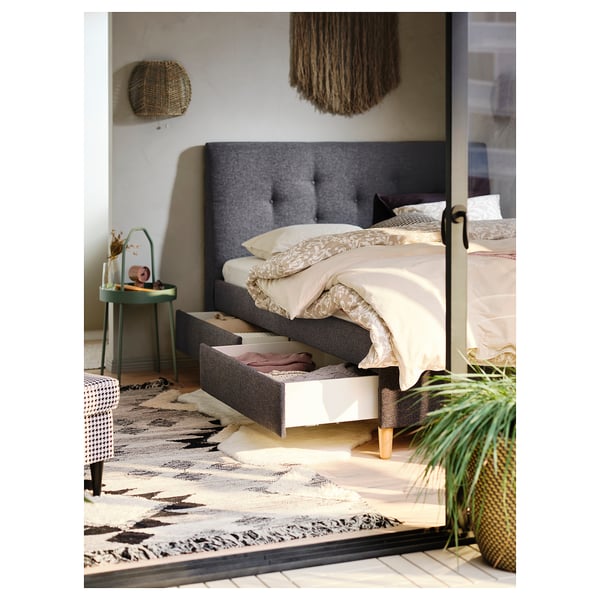Cosy bedroom with grey bed, white linens, green side table, large rug.