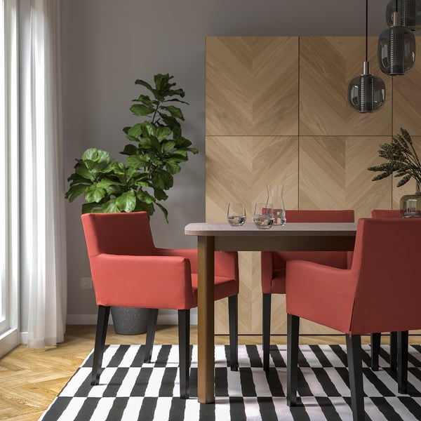 Modern dining setup with wooden table, red cushioned chairs, wine glasses, plant, and striped rug.