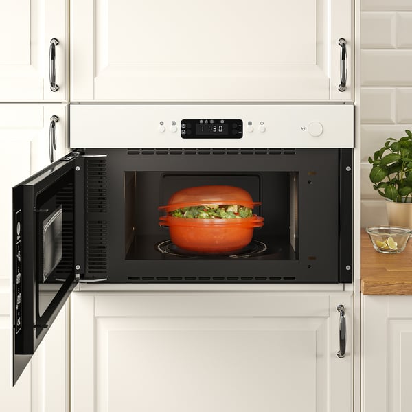 Microwave with a covered dish inside, placed in a white kitchen cabinet, ready for cooking.