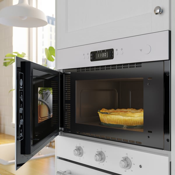 Open white microwave with golden pie. Digital display, silver knobs.