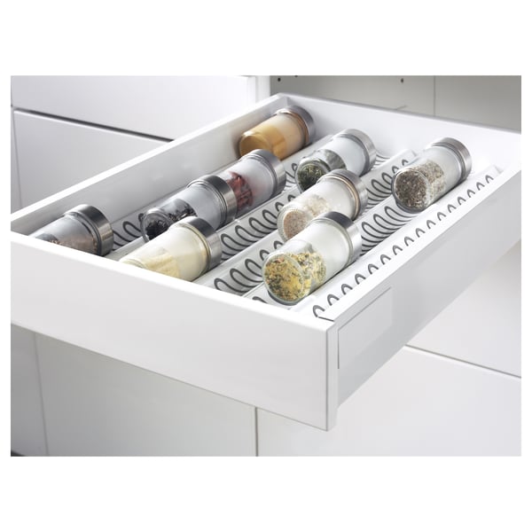 A white kitchen drawer organiser holds six spice jars, each labelled and secured with spring-loaded holders to prevent spills.