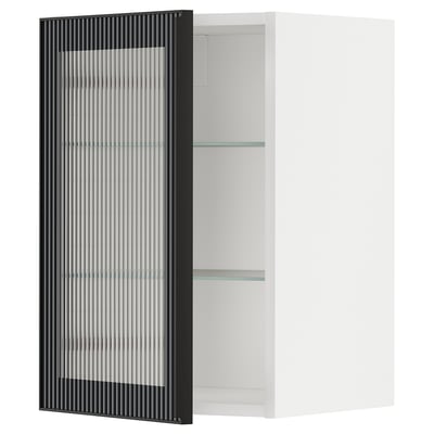 A white METOD kitchen cabinet with a black glass door featuring a reeded design. The cabinet has two glass shelves.