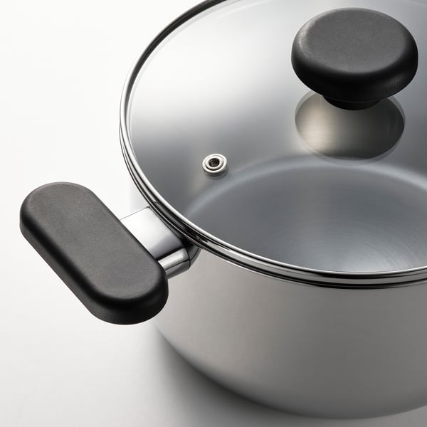 Modern stainless steel saucepan with glass lid, black handles, ready for cooking.