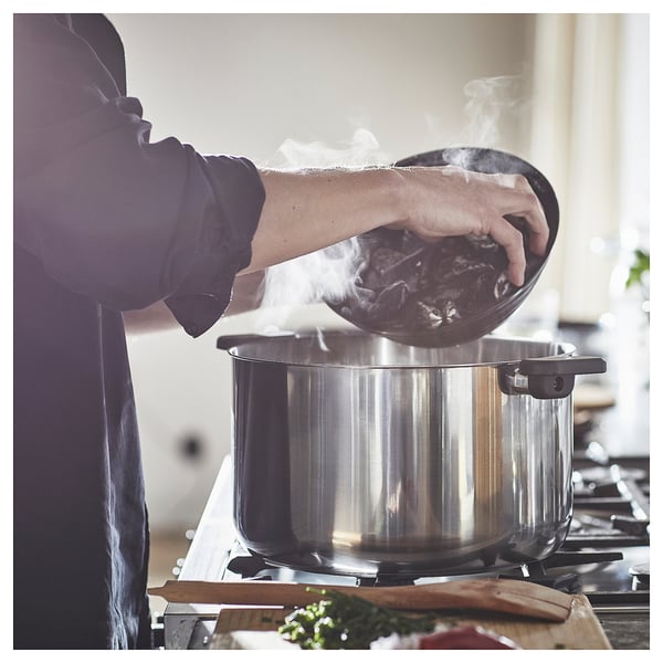 Person cooking on stove with steam, herbs nearby.