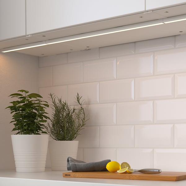 Modern kitchen with under-cabinet lighting, plants, lemon, and knife on counter.