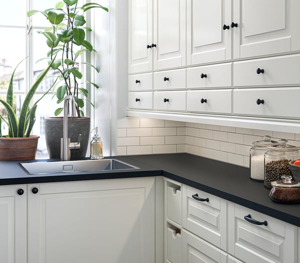 Modern kitchen with white cabinets, black countertop, stainless steel sink, plants, and jars.